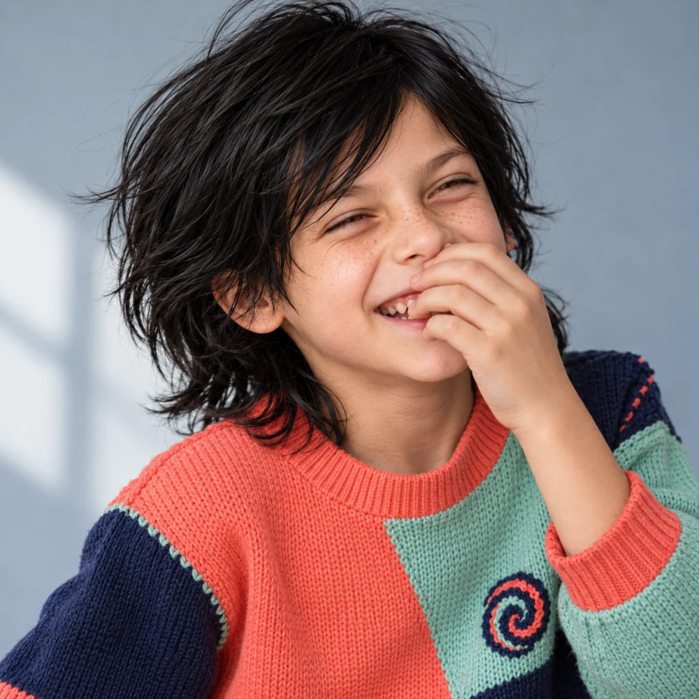 Giggling with one hand near the mouth in a coral, mint and navy sweater